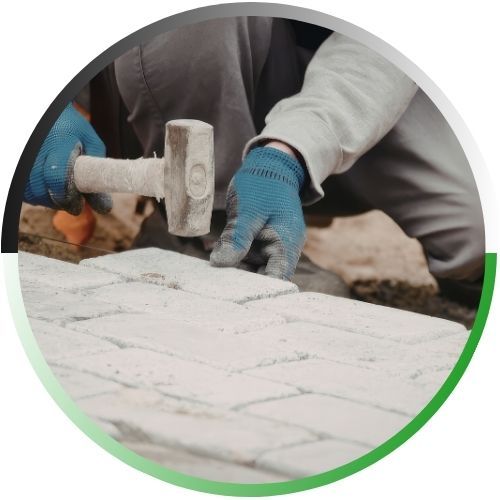 Circular icon showing a worker’s hands using a rubber mallet to precisely set stone pavers into a new patio surface.