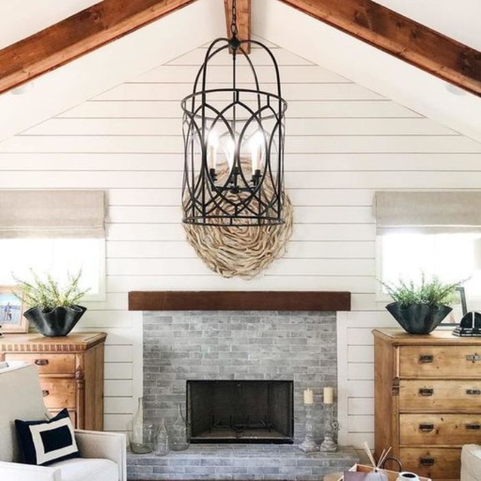 A large, black lantern-style pendant light hangs in a bright living room with a vaulted ceiling and a gray brick fireplace A large, black lantern-style pendant light hangs in a bright living room with a vaulted ceiling and a gray brick fireplace