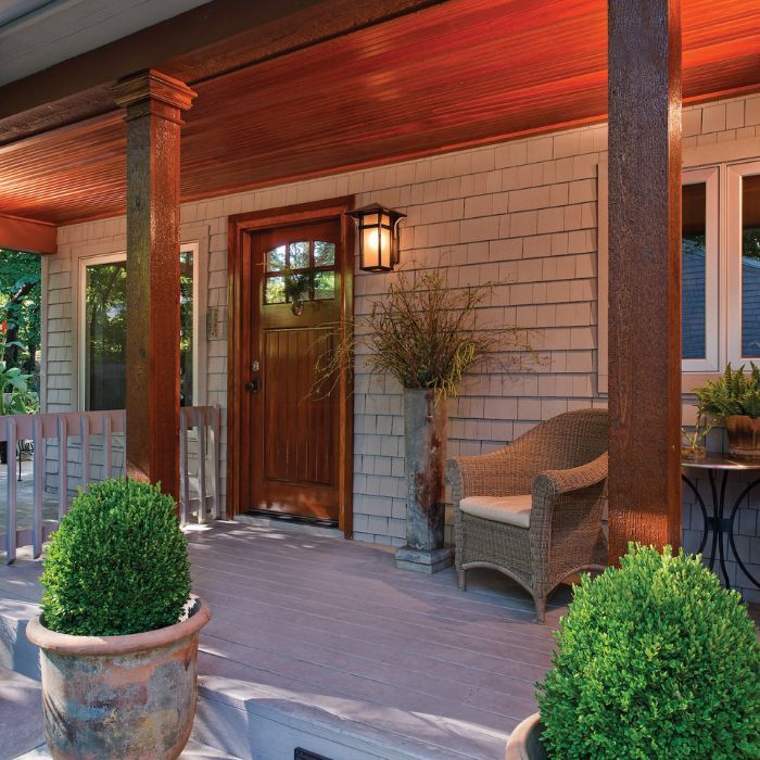 A welcoming cabin front porch with a lit, rustic lantern-style sconce next to a rich wood door and a wicker chair. A welcoming cabin front porch with a lit, rustic lantern-style sconce next to a rich wood door and a wicker chair.