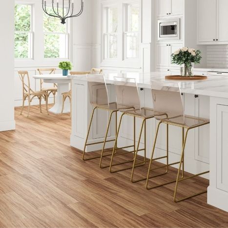Bright white kitchen with modern brass bar stools at a large island and light luxury vinyl plank flooring.