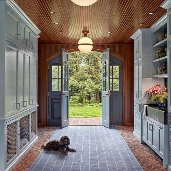 A dog rests in a cozy mudroom with wood-paneled walls, light blue cabinets, and two globe pendant lights hanging from the ceiling. A dog rests in a cozy mudroom with wood-paneled walls, light blue cabinets, and two globe pendant lights hanging from the ceiling.