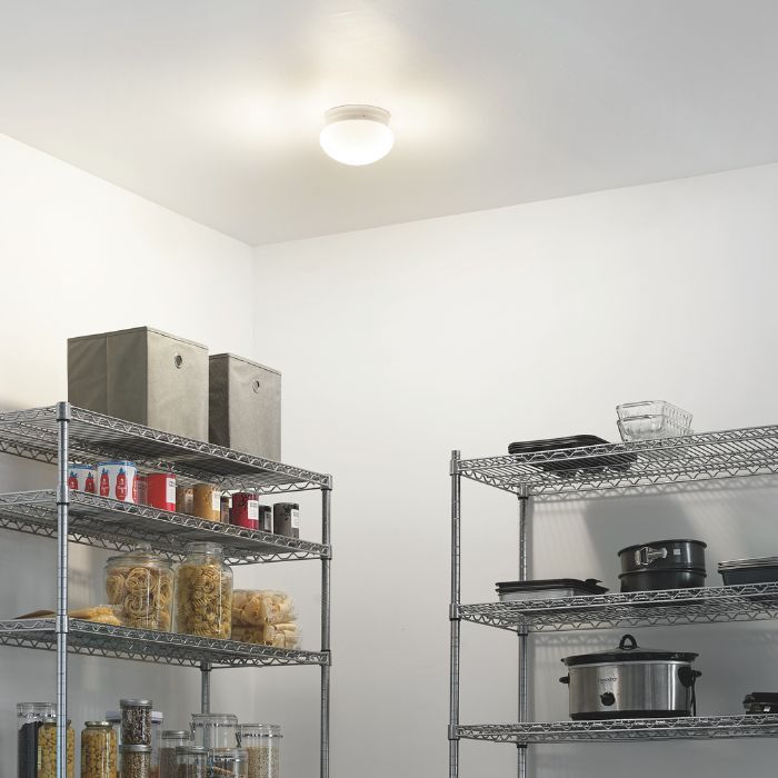 A simple, round flush-mount utility light illuminates a storage pantry filled with wire shelving units.