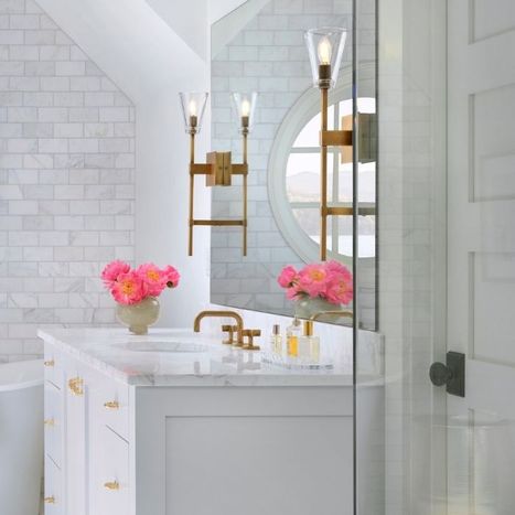 Bright bathroom vanity area with a round mirror flanked by brass sconces, decorated with pink flowers.