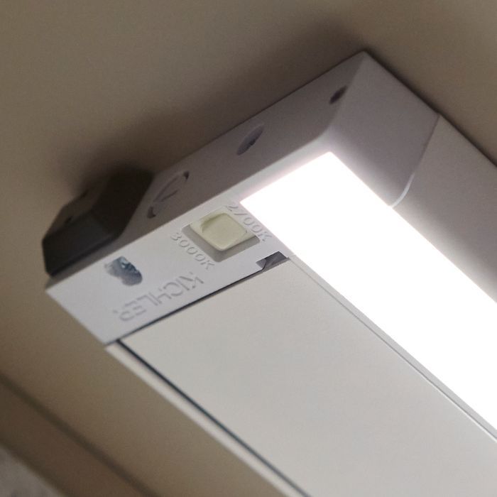 A close-up view of a white LED under-cabinet light bar, showing the switch to adjust light color temperature.
