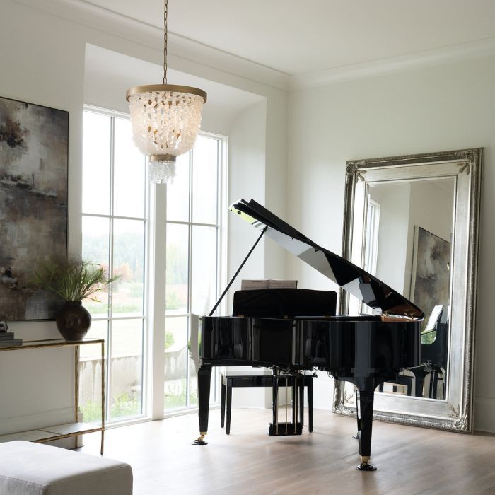 An elegant, light-filled room with a black grand piano. A cascading crystal chandelier with a gold frame hangs near a large window, providing a beautiful focal point. A large, ornate silver mirror leans against the far wall. An elegant, light-filled room with a black grand piano. A cascading crystal chandelier with a gold frame hangs near a large window, providing a beautiful focal point. A large, ornate silver mirror leans against the far wall.