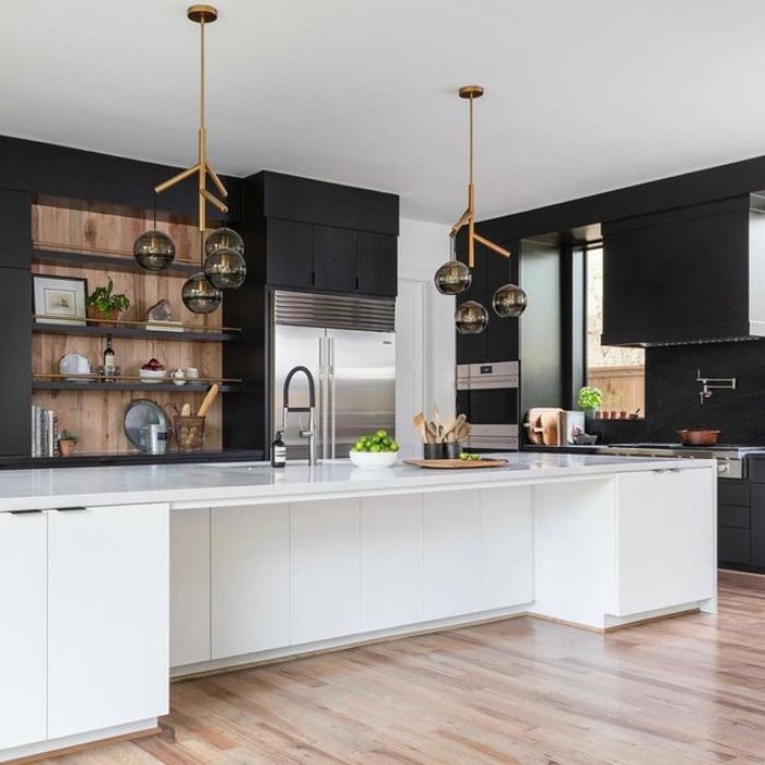 Two modern brass chandeliers with smoked glass globes illuminate a white island in a contemporary kitchen with black cabinets and wood accents. Two modern brass chandeliers with smoked glass globes illuminate a white island in a contemporary kitchen with black cabinets and wood accents.