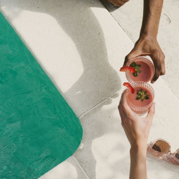 "cheers" drinks on concrete deck by green pool