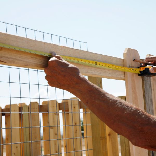 Person measuring a section of a wooden fence
