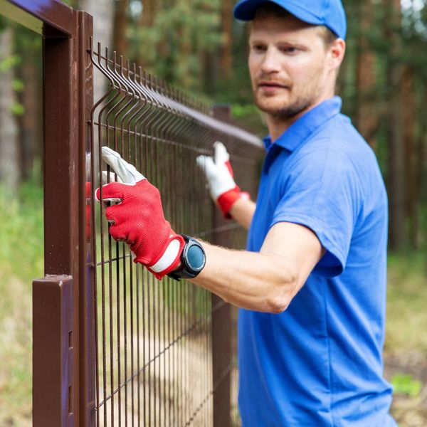 Man in blue installing a fence. 