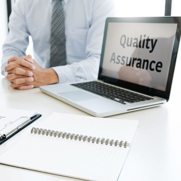 Person sitting next to a computer screen with the words "Quality Assurance" on it. 