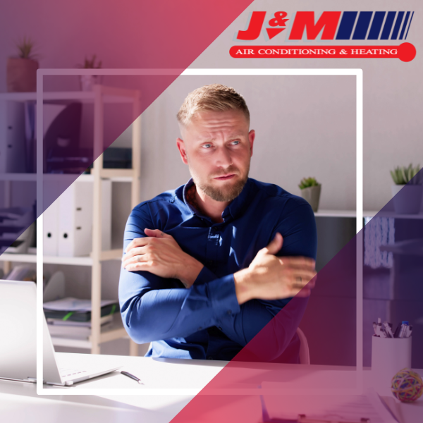 A man sitting at a desk holding his arms like he is cold. 