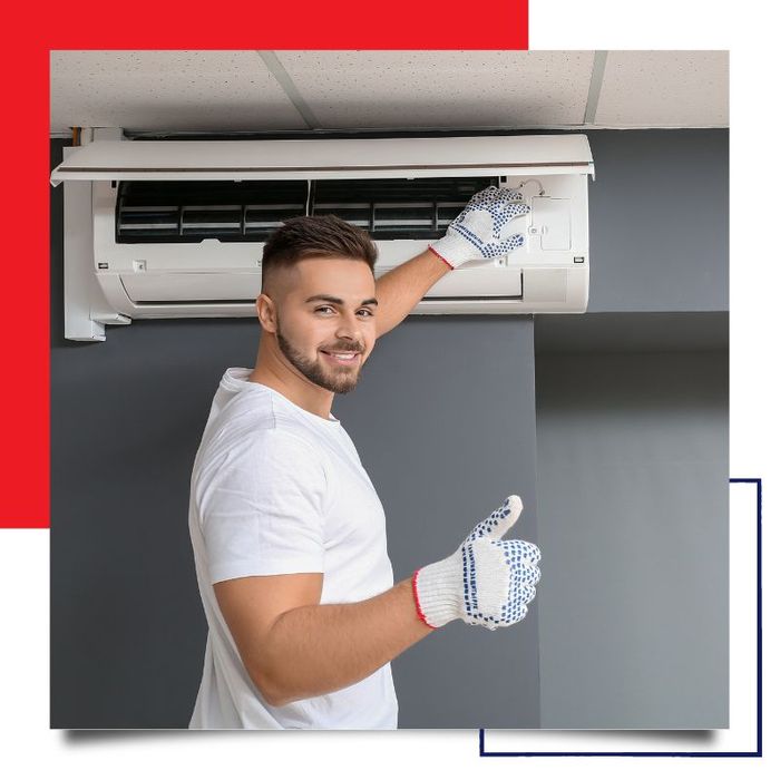 HVAC technician giving a thumbs up while working on a wall-mounted AC unit