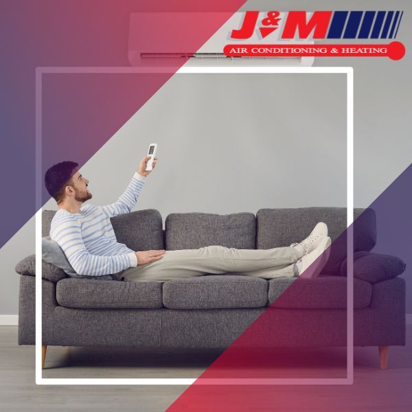 Man sitting on a couch using a remote to activate a mini split ac unit