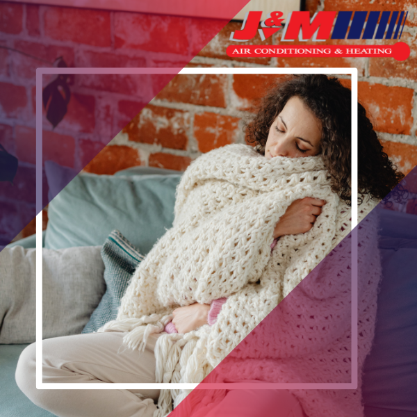 A woman snuggling in blankets on a couch to stay warm 