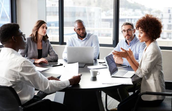 a group of business people talking at a table in front of computers and paperwork