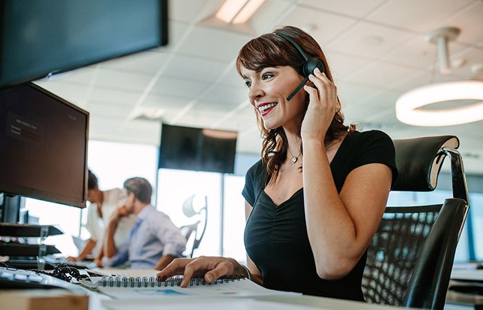 a business woman taking a call in a headset in front of a computer