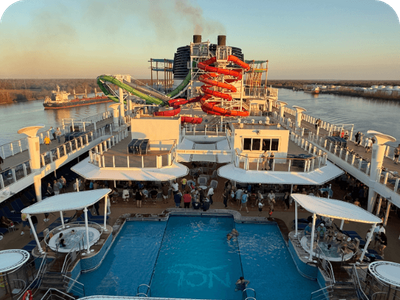 The vibrant pool deck of a cruise ship with large water slides at sunset, showcasing a fun cruise vacation.