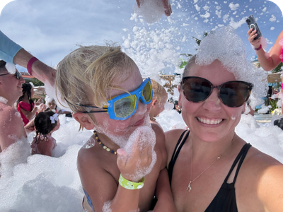 A mother and son smiling and laughing while covered in bubbles at a resort foam party.