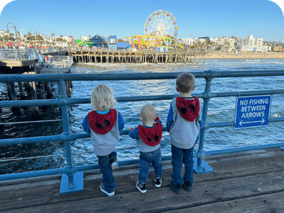 Three young children in matching hoodies looking out at the ocean from the Pier, a popular family travel destination.