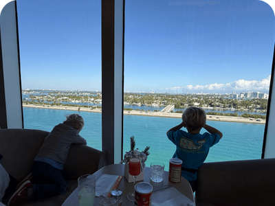 Two young boys looking out a large window at the ocean and a coastal city during a family vacation.