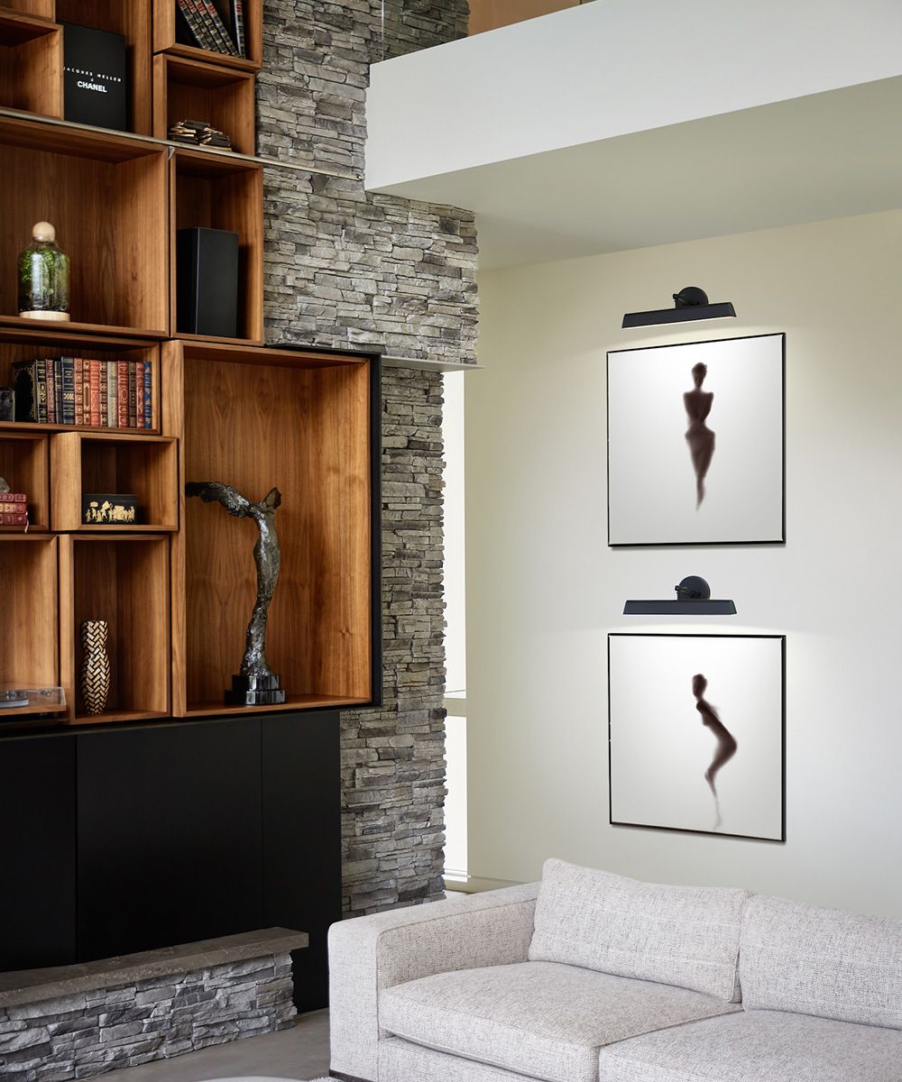 A black picture light sconce above minimal black and white pictures in a luxury living space