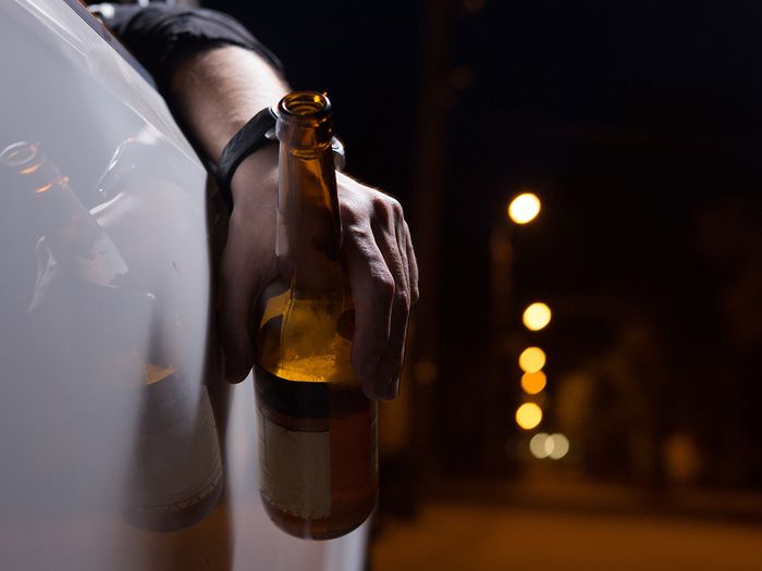 photo of man holding beer with his arm hanging outside car window