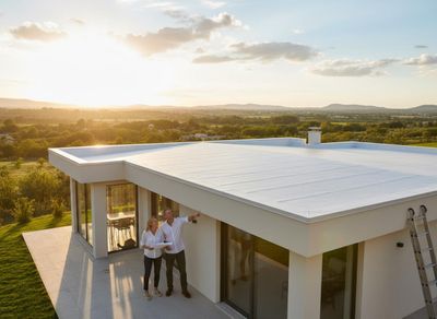 Couple inspecting modern house with flat white roof at sunset