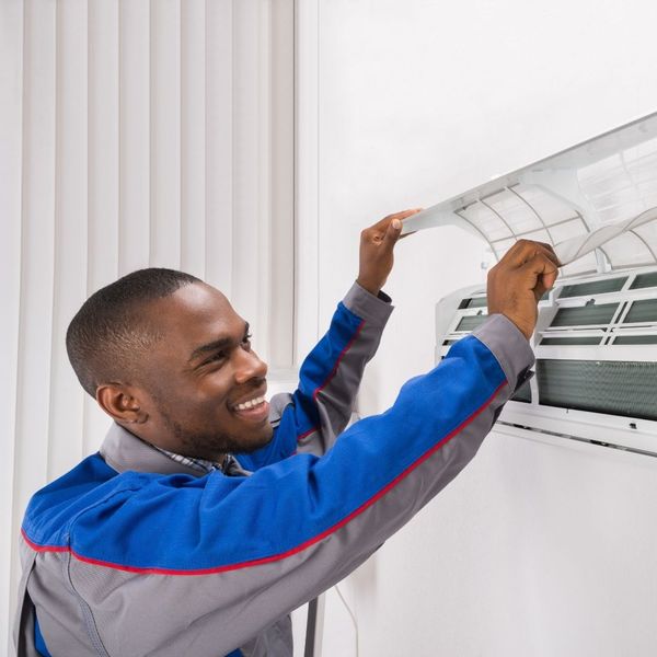 Smiling, professional HVAC technician in uniform inspecting a mini-split indoor unit. Smiling, professional HVAC technician in uniform inspecting a mini-split indoor unit.