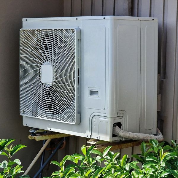 Outdoor mini-split condenser unit mounted on a bracket, surrounded by greenery. Outdoor mini-split condenser unit mounted on a bracket, surrounded by greenery.