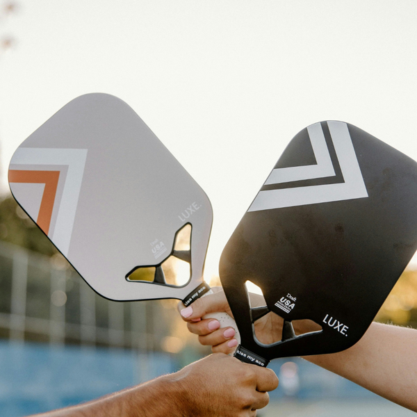 Two players crossing their pickleball paddles together on a sunlit court. Two players crossing their pickleball paddles together on a sunlit court.