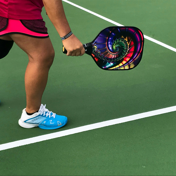 A player on a green pickleball court holding a paddle with a vibrant, artistic design. A player on a green pickleball court holding a paddle with a vibrant, artistic design.