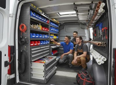 A team of three service technicians examines the custom storage solutions, including bins, drawers, and tool racks, inside a white work van. Service Professionals in Organized Work Van
