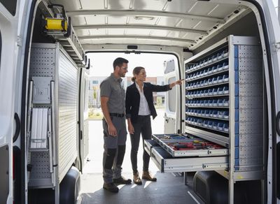 Two technicians examine a custom-fitted cargo van with organized shelves, bins, and pull-out tool drawers for mobile work. Professionals Reviewing Organized Cargo Van Storage