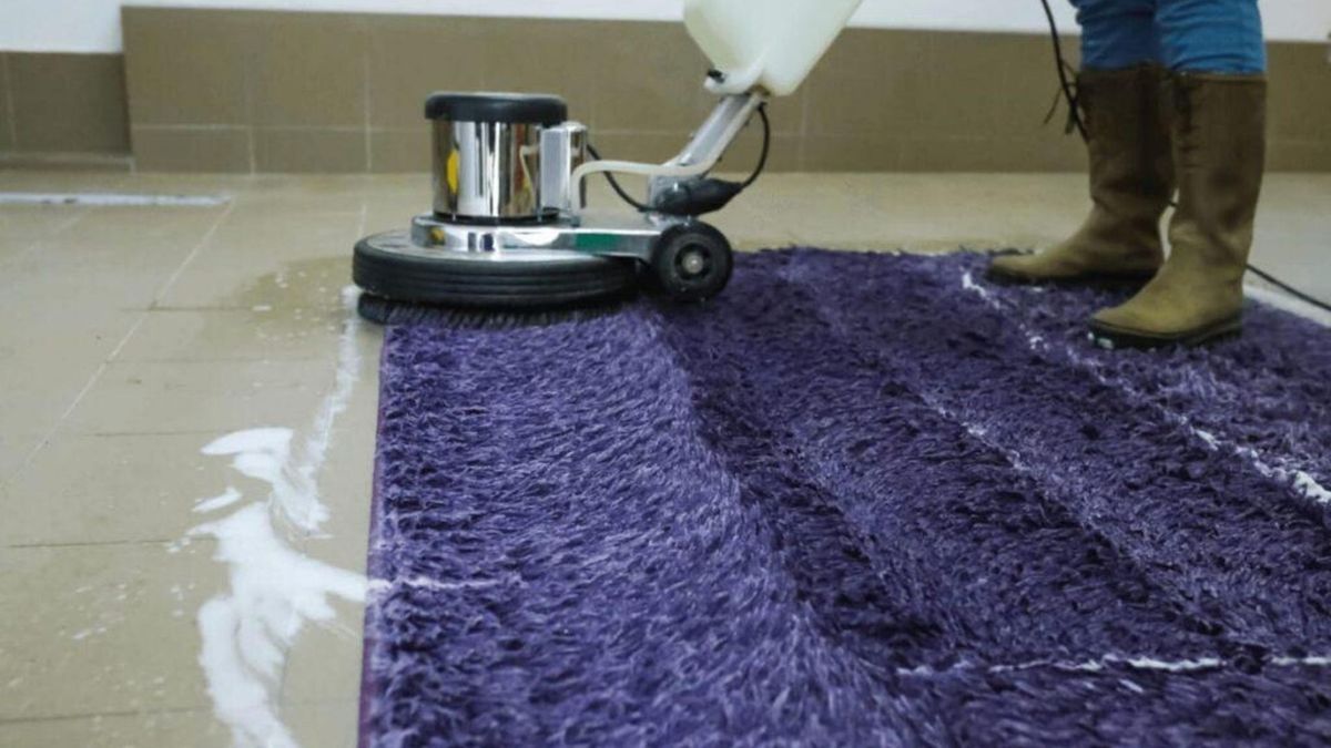 A rotary carpet cleaning machine is being used to clean a fluffy purple area rug