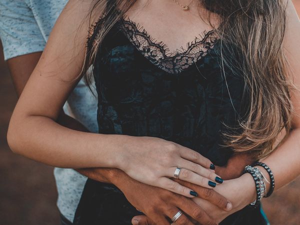 Close up of woman standing in front of her partner with his arms wrapped around her