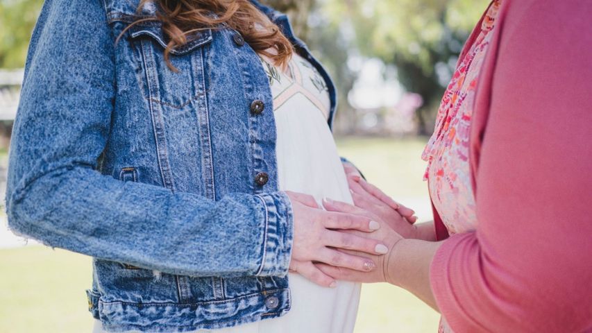 A woman gently touching another woman's baby bump