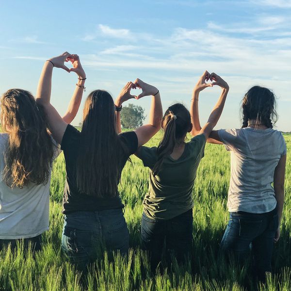 Young woman standing in a field creating heart shapes with their hands.