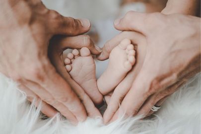 father and mothers hands around baby feet Surrogacy Process.jpg