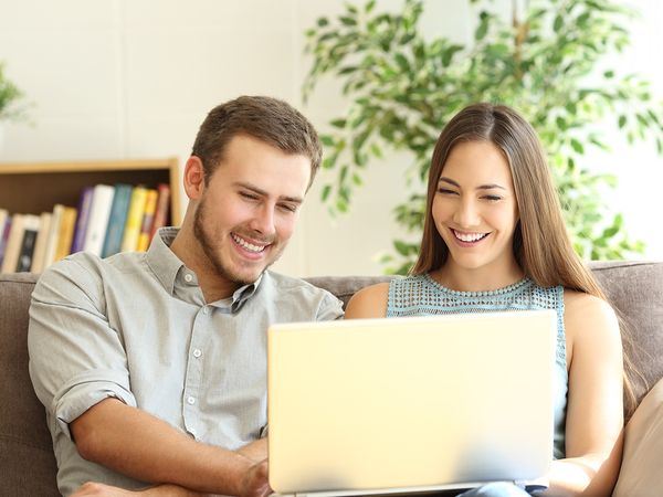 A young couple smiling at a surrogate’s profile on their laptop.