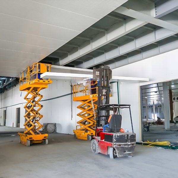 Workers using scissor lifts to install ceiling panels indoors.