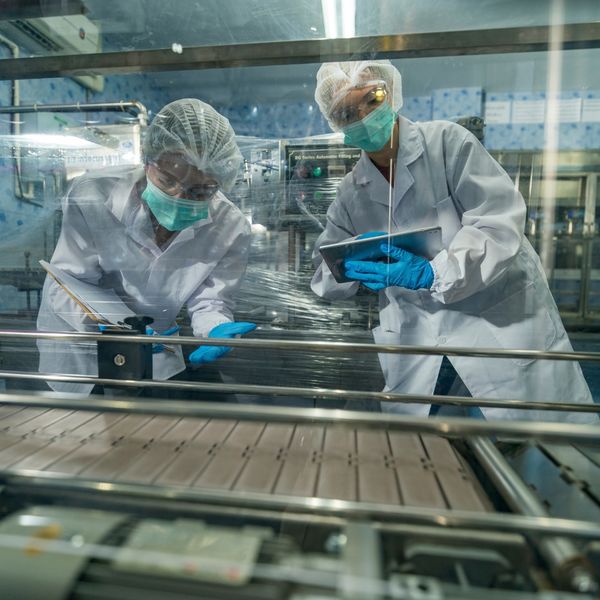 Two technicians in lab gear inspecting a production line.
