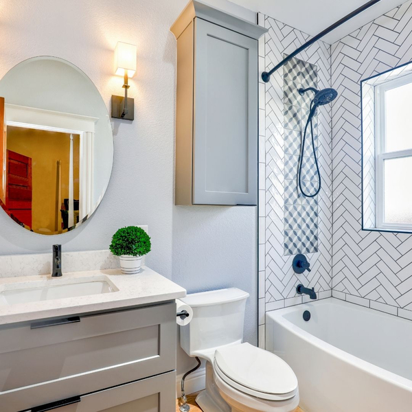 white herringbone tile shower, oval mirror, grey cabinets