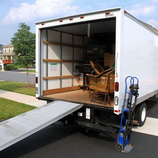 Back of a moving truck with a ramp extended and a blue hand truck. Back of a moving truck with a ramp extended and a blue hand truck.