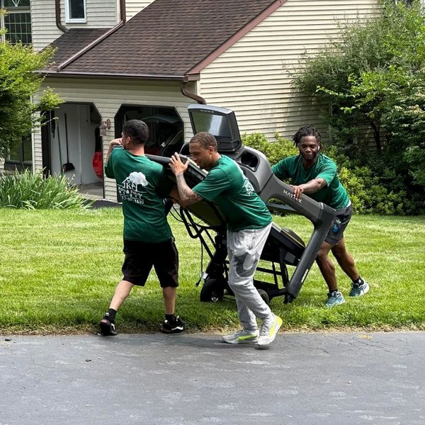 Three movers carrying a heavy treadmill across a lawn. Three movers carrying a heavy treadmill across a lawn.
