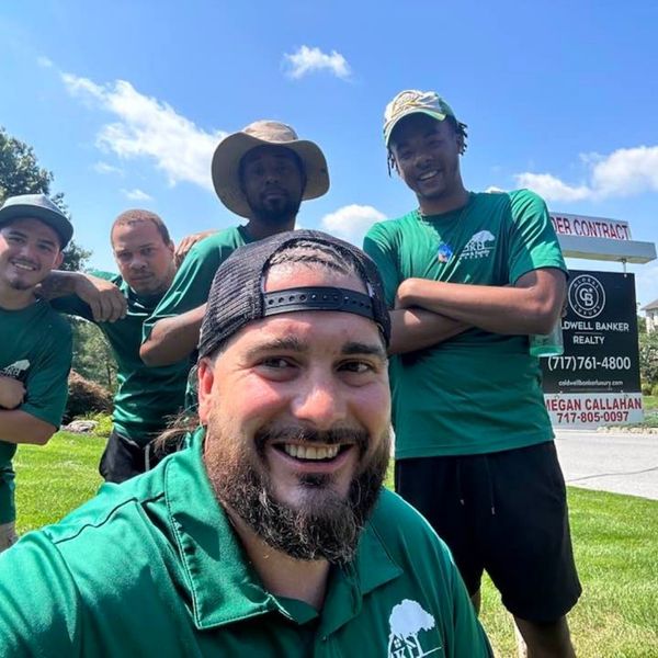 Group selfie of five Kane and Family movers in green shirts outdoors. Group selfie of five Kane and Family movers in green shirts outdoors.