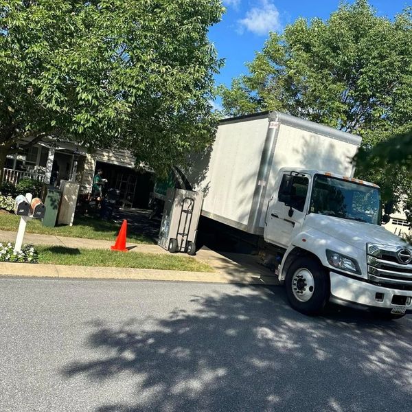 A professional white moving truck with its loading ramp extended, parked on a quiet residential street in Dallastown for a home relocation. A professional white moving truck with its loading ramp extended, parked on a quiet residential street in Dallastown for a home relocation.