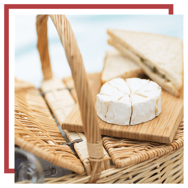 Image of a picnic basket with a cutting board, brie, and a sandwich