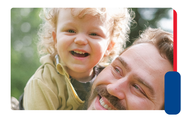A young child sitting on his father's shoulders smiles at the camera