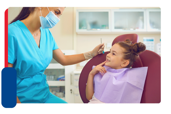 Young girl in dentist chair motioning at her mouth to a hygienist
