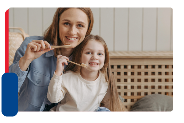 A mother and her young daughter smile and hold up tooth brushes to their mouths